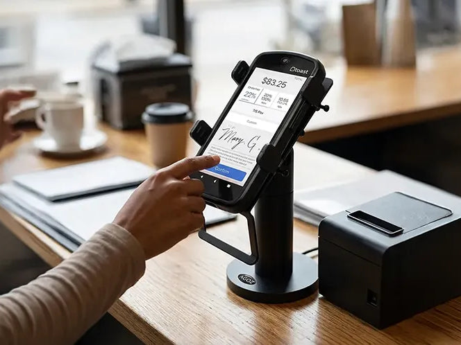 Customer using a mounted Toast Go 2 payment terminal on a checkout counter beside a receipt printer in a retail or café setting.