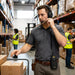 Warehouse worker wearing a headset with a Honeywell Voice terminal secured in an AgozTech snap closure case on a waist belt while handling fulfillment boxes in a warehouse aisle.