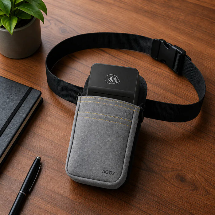 A gray fabric belt pouch with a black Adyen card reader device inserted, shown on a wooden desk with a notebook, pen, and plant nearby. The pouch has a visible AGOZ logo.