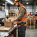 Worker wearing a Janam mobile computer waist belt holster while packing orders at a warehouse workstation during long-shift scanning tasks.