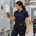 Electrical technician checking a Klein Tools digital multimeter while wearing an Agoz utility tool pouch stocked with testing tools at an industrial facility.