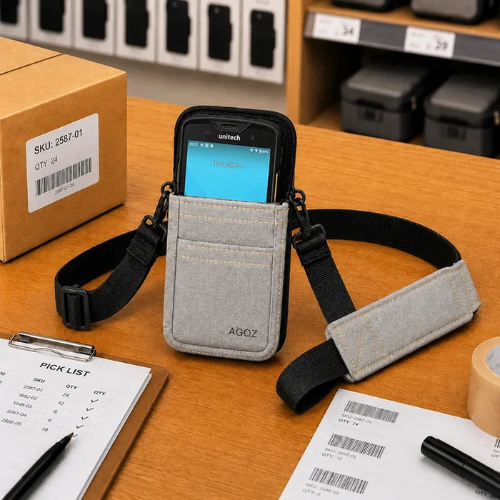 Gray Unitech shoulder sling holster with Unitech device displayed on a packing workstation with barcode paperwork, shipping box, and warehouse supplies.