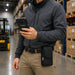 Warehouse worker holding a Bluebird handheld scanner while wearing a compact black AGOZ belt case in a storage aisle.