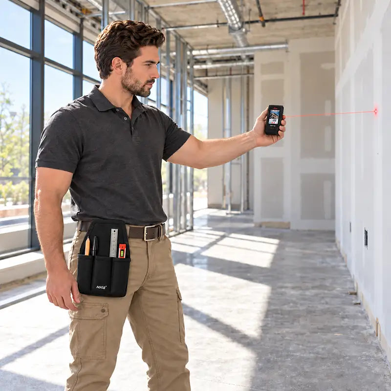 Construction professional using a Leica laser distance meter to measure an interior wall while wearing an Agoz utility tool pouch with measuring accessories on his waist belt.