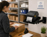 Shipping station employee preparing a package beside a Zebra ZD621 printer mounted on an Agoz swing-arm shelf.