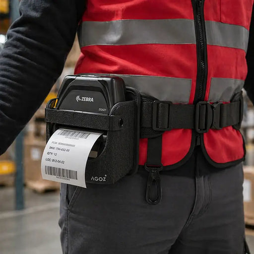 Close-up of an AgozTech Zebra ZQ521 printer waist belt carrying case worn by a warehouse worker in a red safety vest, with a label printing in use.
